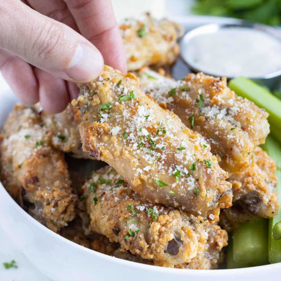 Garlic Parmesan Chicken Wings RECIPE served in a white bowl with ranch and celery on the side.