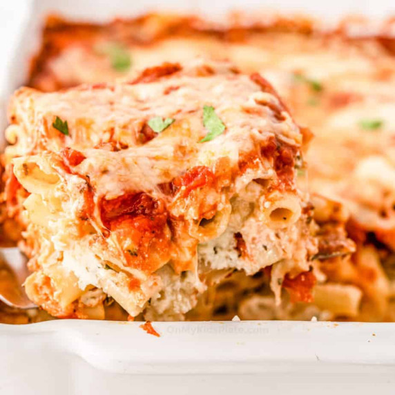 Baked ziti covered in cheese being served from a pan.