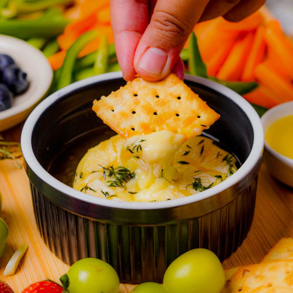 A cracker being dipped into melty baked brie.