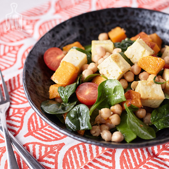 Golden baked halloumi on top of baby spinach, snow peas, cherry tomatoes and chickpeas on plate