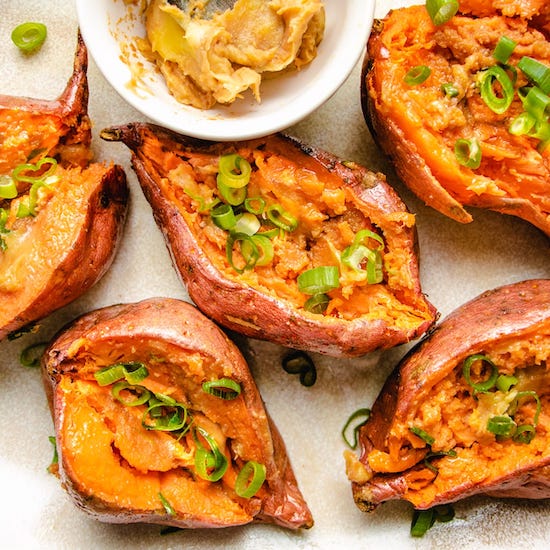 Sliced roasted sweet potatoes with scallions and miso butter in ramekin on white plate