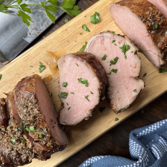 Slices of pork tenderloin on a tan cutting board garnished with minced parsley.