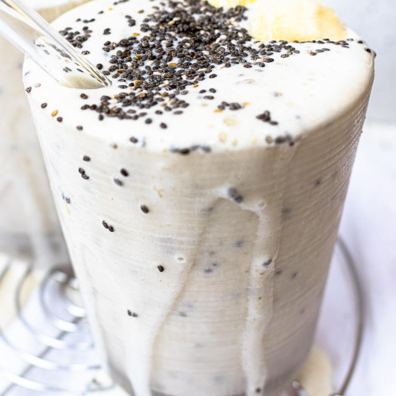 Banana smoothie in a clear cup topped with chia seeds and slices of banana