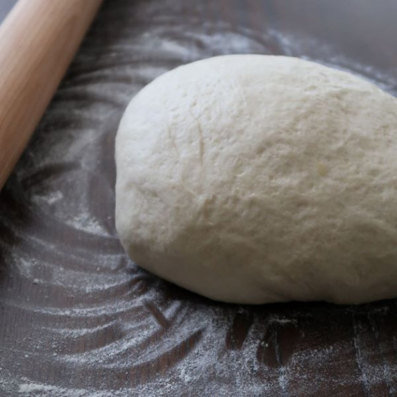 Raw pizza dough on a dark counter with flour and a rolling pin