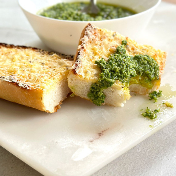 Basil pesto or pesto al basilico in a white bowl with two slices of garlic bread on a marble board