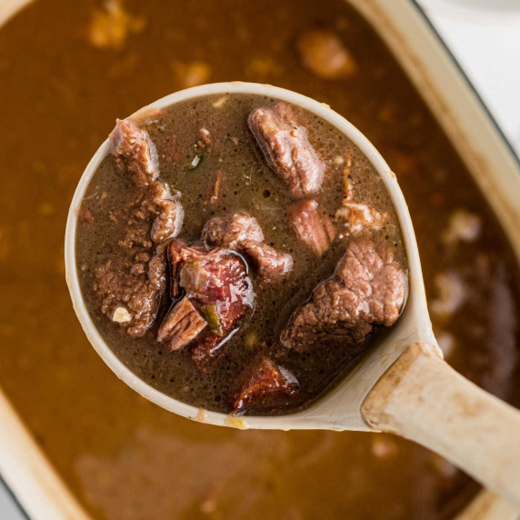 Close up of a ladle full of beef gumbo.