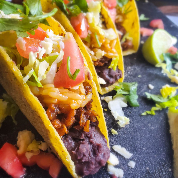 Golden taco shells stuffed with colourful fillings against a black cutting board.
