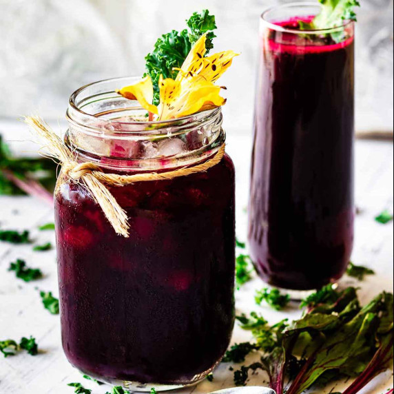 Beet green juice in a jar and a tall glass topped with kale sprigs and a yellow carnation