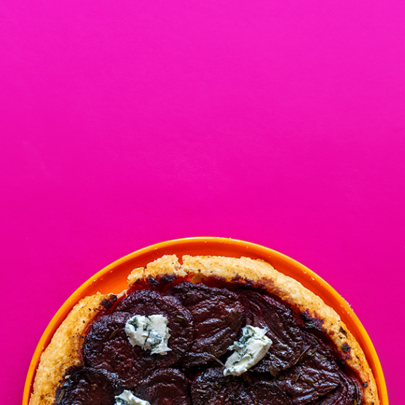 A crescent moon of beetroot tarte tatin on an orange plate and a bright pink backdrop