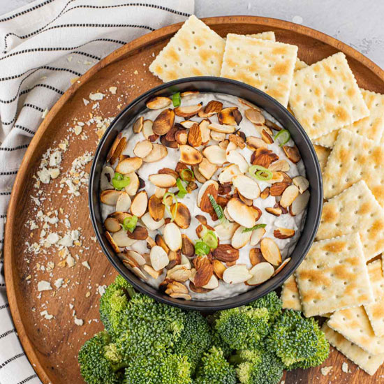 Chicken Dip topped with sliced almonds served with saltine crackers and broccoli over a wood platter