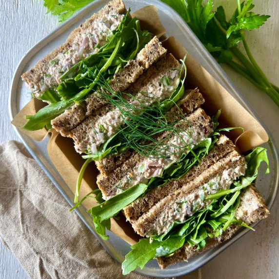 Sandwich halves sitting cut side up in an aluminimum baking tray with herbs around it and napkin.