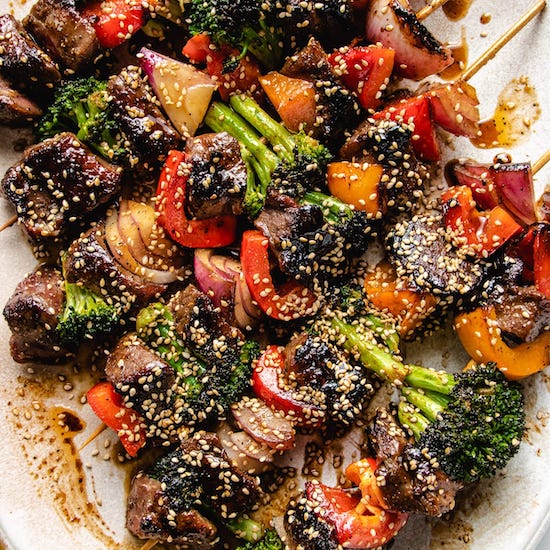Beef kabobs with broccoli, red onion, green pepper and sesame seeds on a white plate