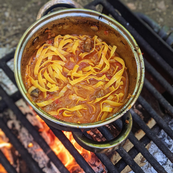 one pot bison bolognese pasta cooking in a small pot over a campfire