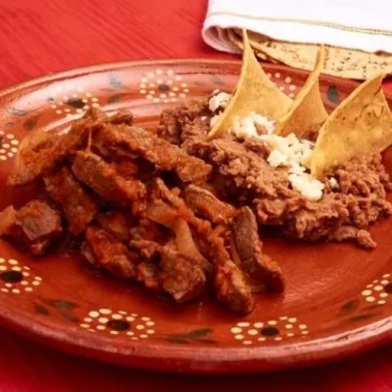 Bistec a la Mexicana with a big stack of warm corn tortillas and refried beans on the side.