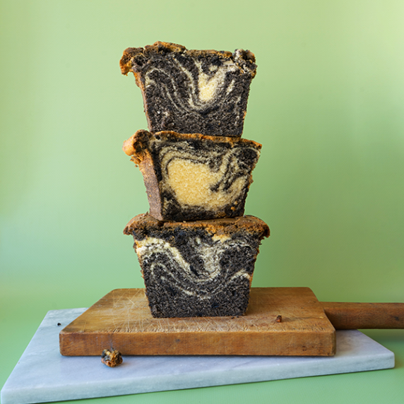 A stack of three slices of pound cake with a black sesame swirl on marble and wooden cutting boards.