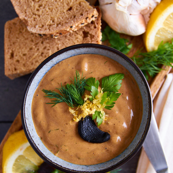 A bowl of black garlic aioli topped with a clove of black garlic, dill and zested lemon