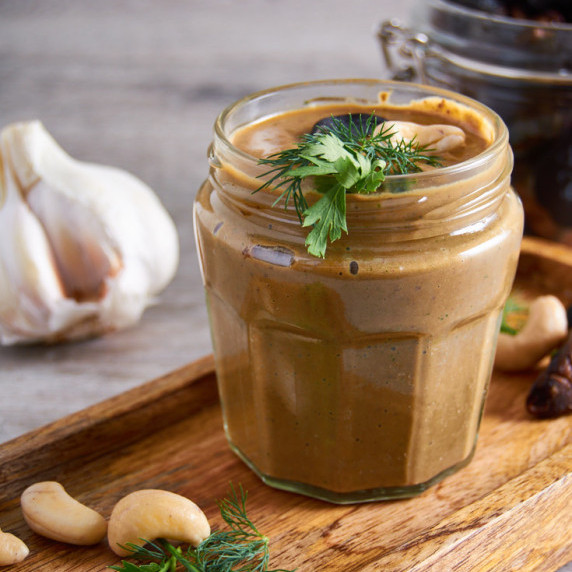 A Jar of Black Garlic Cashew Ranch Dressing topped with fresh herbs on a wooden board.
