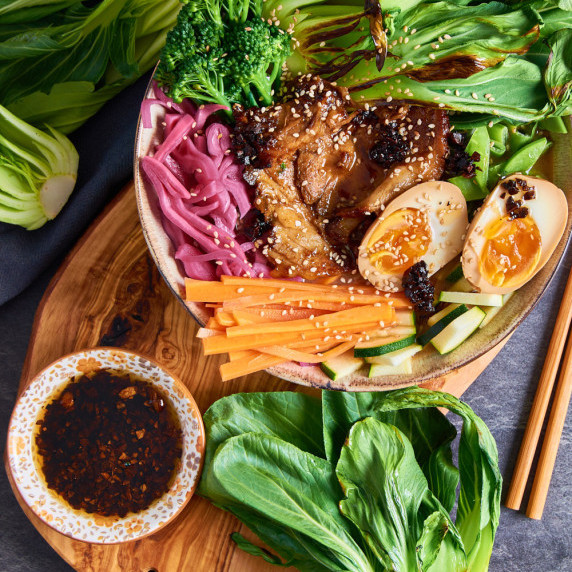 A Black Garlic Pork Ramen bowl topped with Pak Choy, julienned carrots, red cabbage, marinated egg