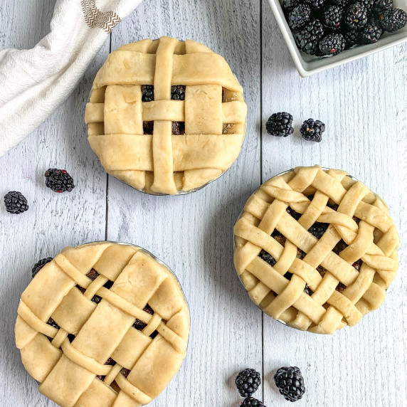 top view of three mini vanilla blackberry pies with lattice tops on a white background