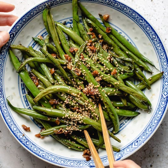 Green beans, garlic and sesame seeds on a white and blue plate with chopsticks