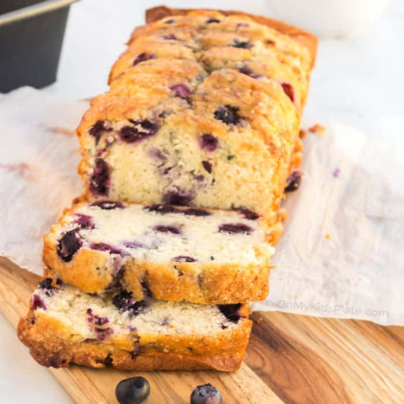 The end of a blueberry loaf, which sits sliced on a cutting board.