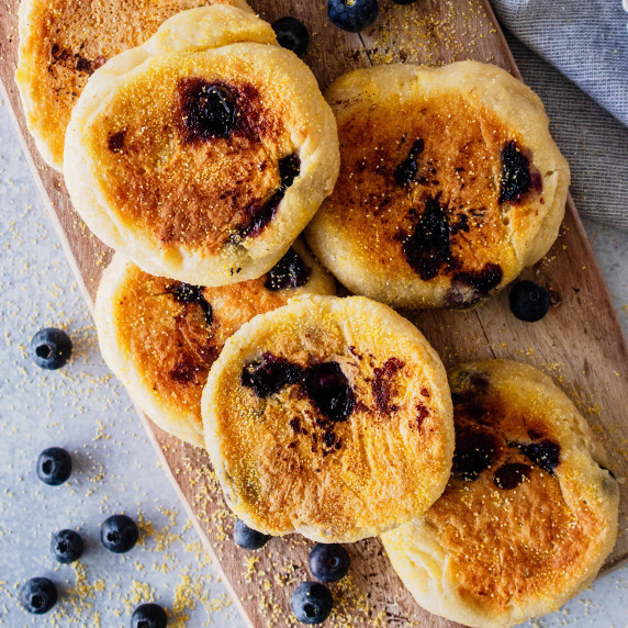 Blueberry English muffins on a wooden cutting board.