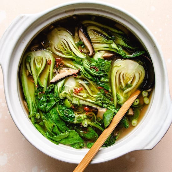 Bok choy soup, red chili peppers, scallions and a wooden spoon in a white stoneware bowl