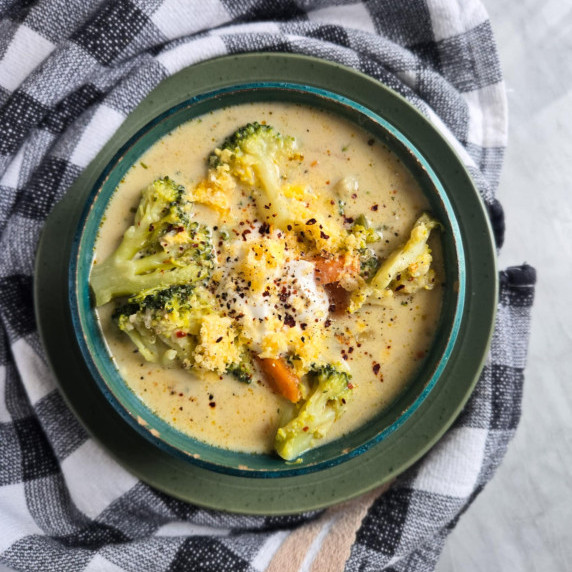 A creamy bowl of broccoli soup against a checkered towel.