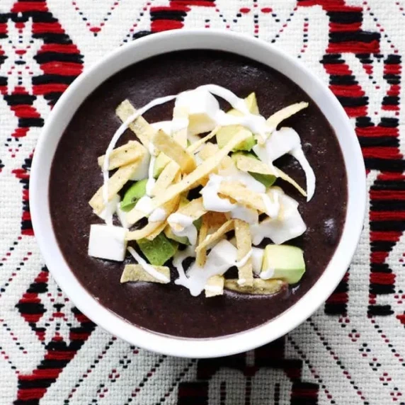 Bowl of black bean soup garnished with tortilla strips, fresh avocado, and queso fresco.