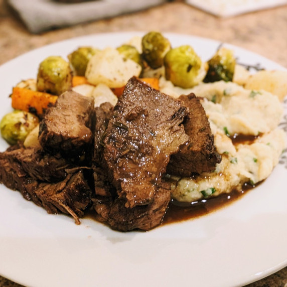 braised brisket on a plate with cauliflower mash, roasted vegetables, and red wine jus