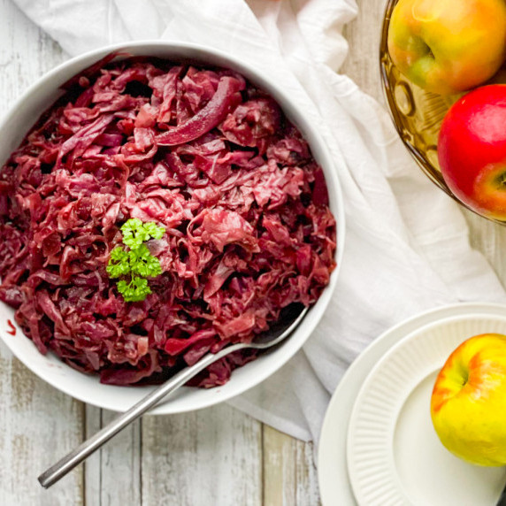 A white bowl filled with red cabbage that is garnished with parsley. A spoon is in the bowl.