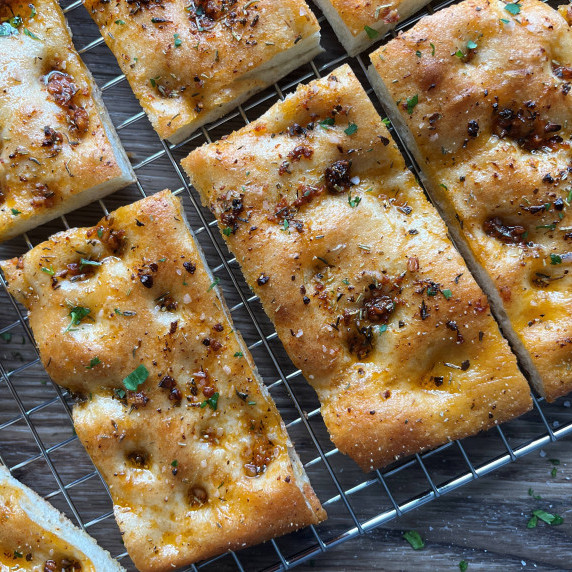 Slices of focaccia bread garnished with fresh parsley and kosher salt on a wire cooling rack.