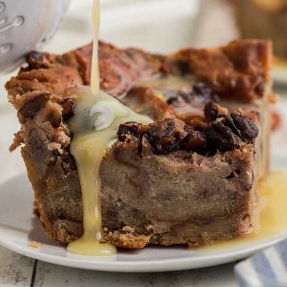 Close up of a slice of bread pudding with rum sauce being poured over the top.