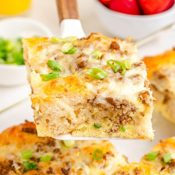 A slice of breakfast biscuit casserole with sausage, egg and cheese being lifted from the pan.