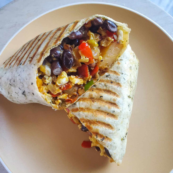 A golden brown burrito stuffed with a fluffy yellow scramble with pops of black and greens.