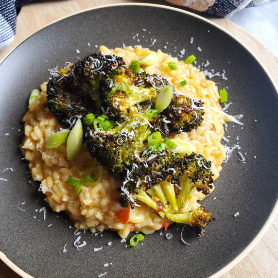 Green roasted broccoli on creamy risotto on a matte plate with a checkered towel in the background.