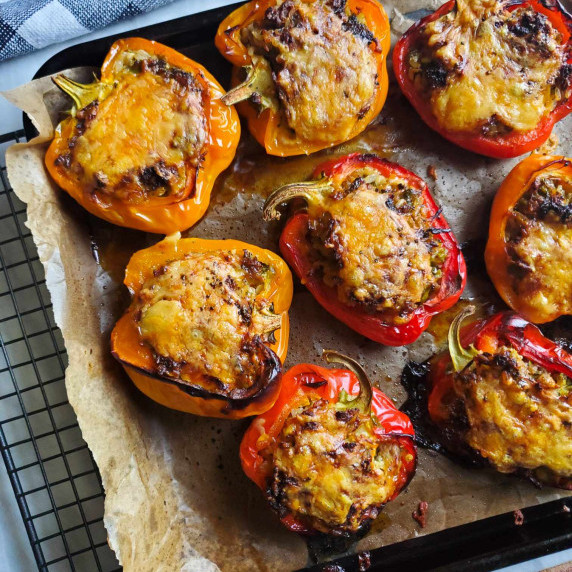 A sheet pan of orange and red baked peppers with a checkered towel in the background.