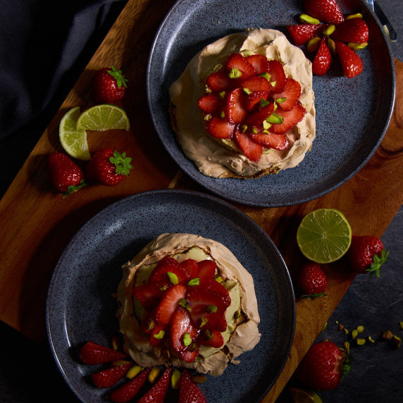 Two Brown Sugar Pavlovas with Pistachio Protein Mousse and Strawberries on dark blue plates.
