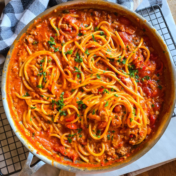 A skillet full of red sauced bucatini pasta and pops of green herbs.