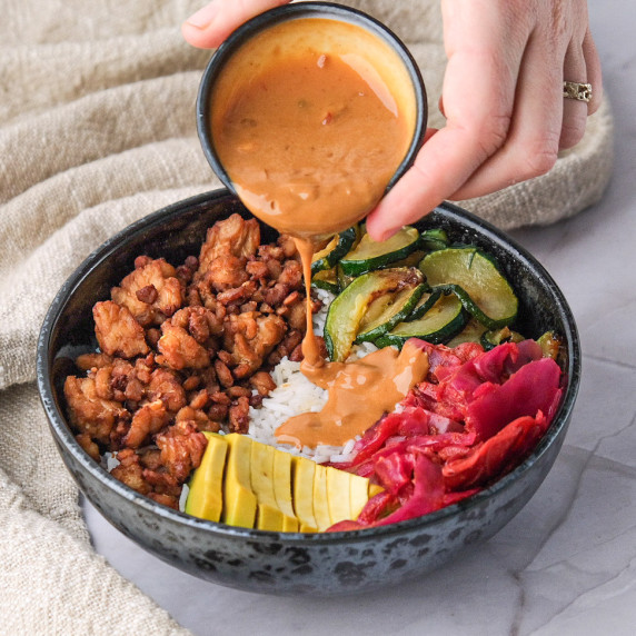 Someone pouring peanut butter buddha bowl dressing into a Buddha bowl 