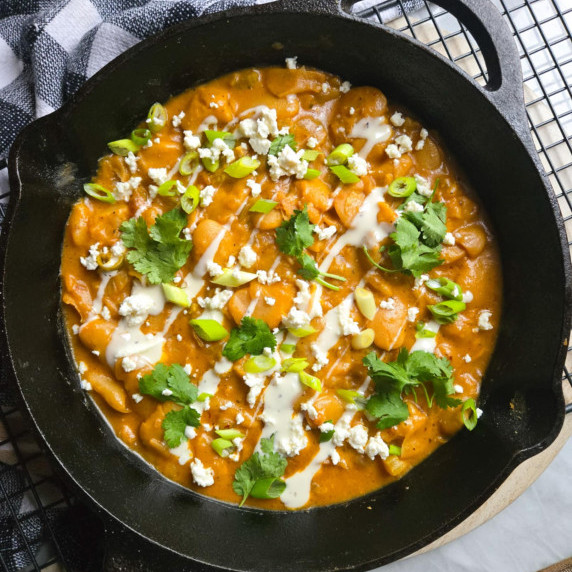 A skillet full of buffalo beans drizzled with white Ranch and green cilantro and onions