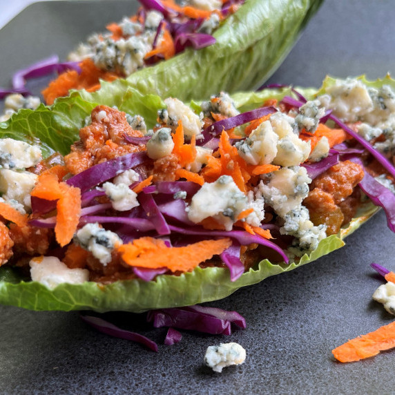 Spicy buffalo chicken in a lettuce wrap topped with shredded carrot, red cabbage, and blue cheese.
