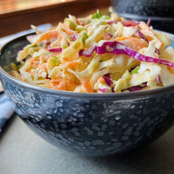 Coleslaw made with red and green cabbage, carrot, and onion in a gray bowl on a slate cutting board.