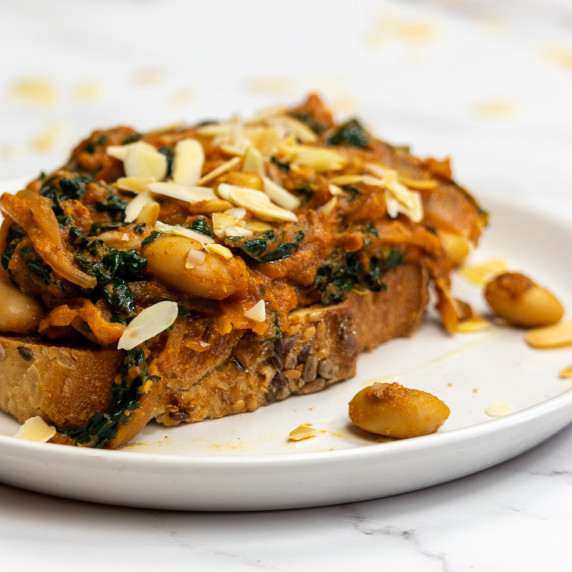 Butter Bean Curry on toast topped with flaked almonds on a white plate