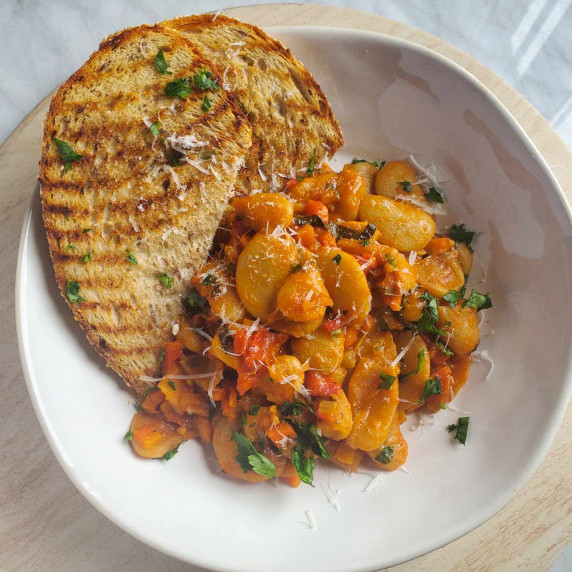 A white bowl filled with an orange hued sauté of beans and golden grilled toast.