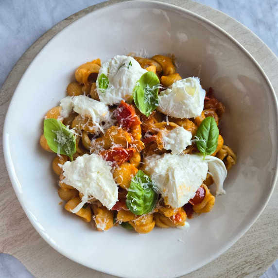 Red sauced pasta in a white bowl with green basil and creamy white burrata