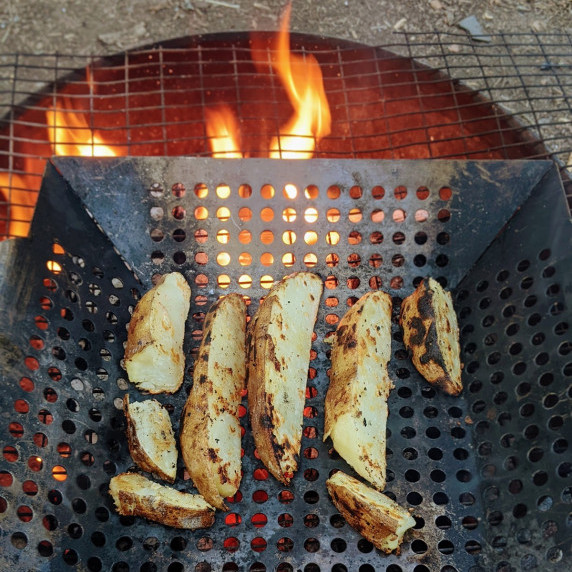 potato wedges cooking in a grill basket over a campfire