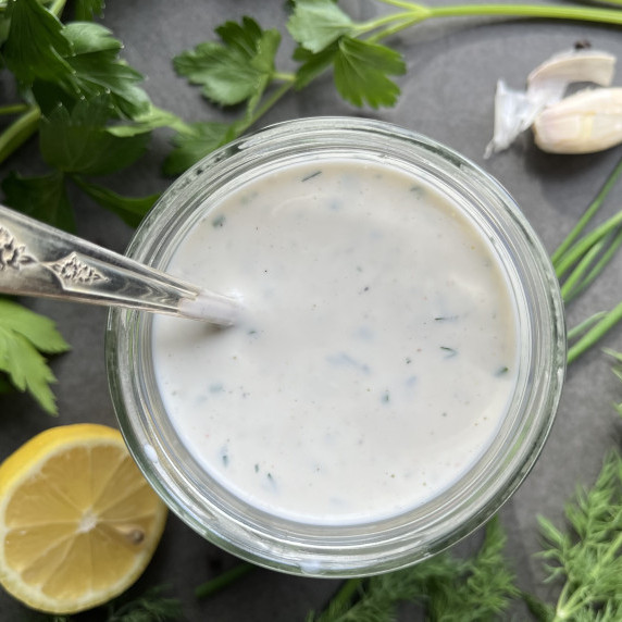 Jar with ranch dressing surrounded by fresh herbs and a lemon slice.