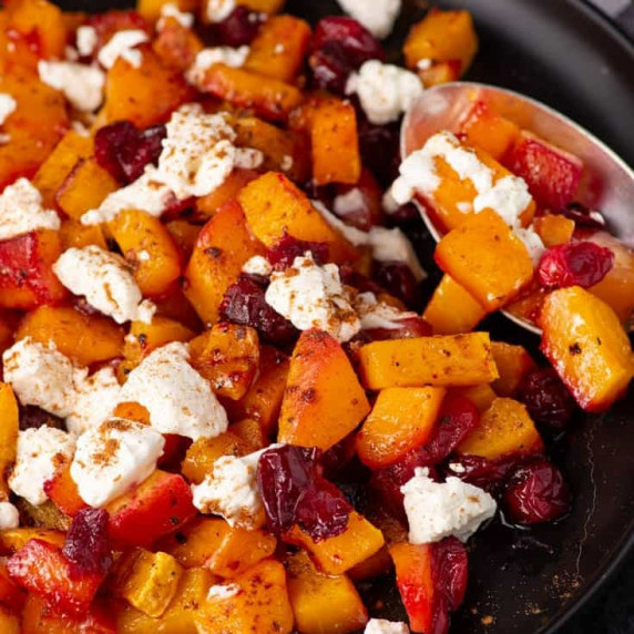 A black platter with roasted butternut squash with cranberries and feta