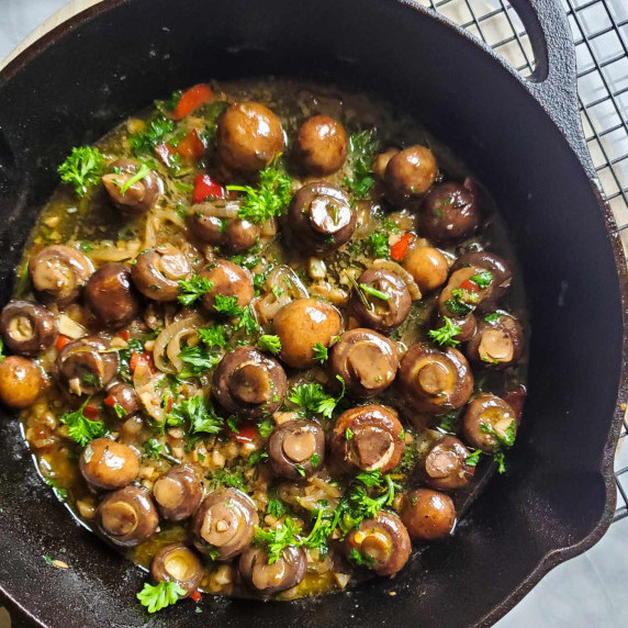 A skillet full of saucy mushrooms and fresh green herbs.